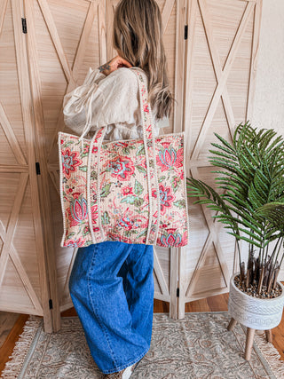 Person holding a floral tote bag in front of a wooden door with plants in the background