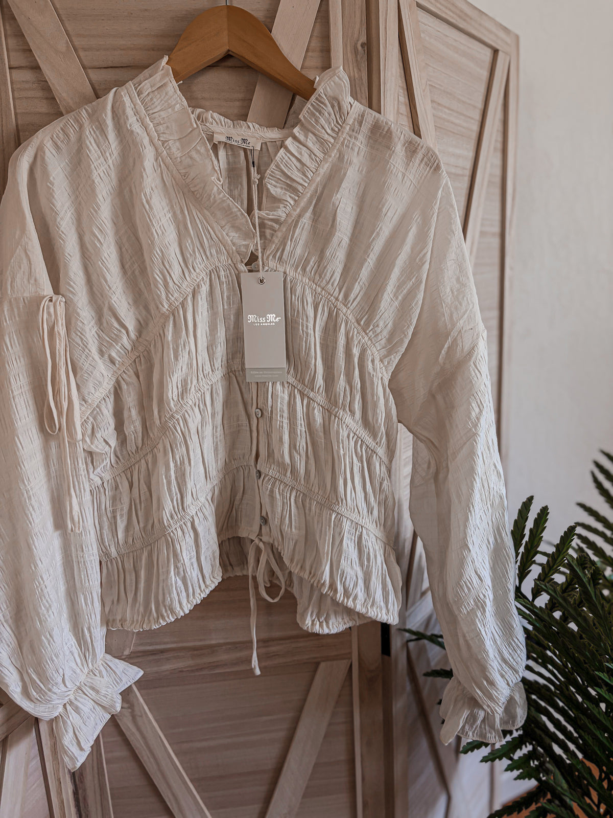 cream textured blouse on a hanger with a plant in the background