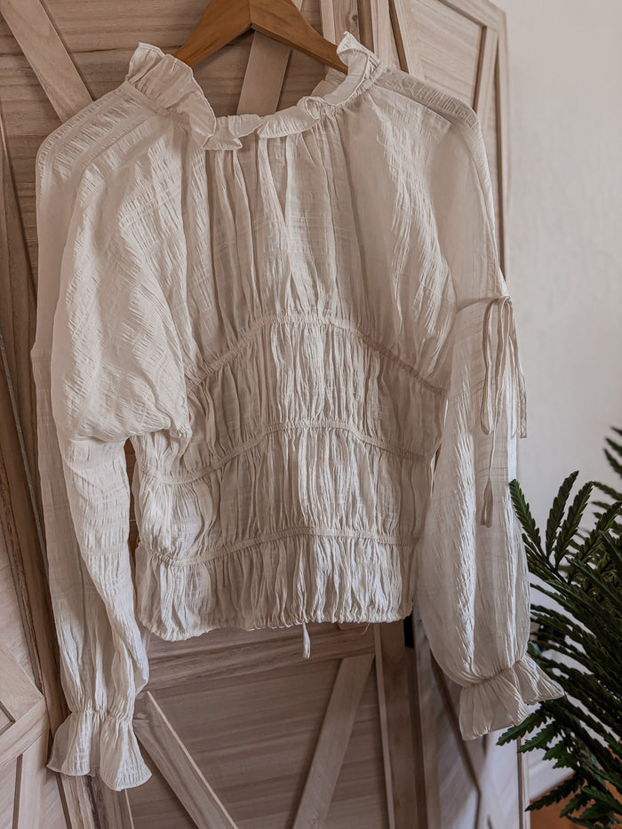 cream blouse on a hanger against a wooden panel background